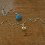 Close-up of a vintage mini Givenchy heart charm necklace, featuring an authentic gold-toned heart pendant on a delicate enamel colored blue chain. A rare and timeless piece, repurposed for modern wear, blending classic elegance with effortless everyday luxury