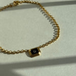 Reworked vintage Dior pendant necklace featuring an octagonal gold frame with black enamel center and white Dior monogram, suspended on a gold rolo chain, styled flat on a soft white fabric background
