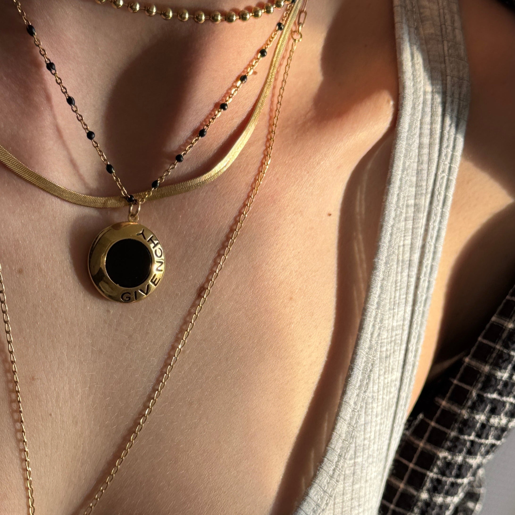 Close-up of a person wearing a gold vintage Givenchy necklace with a black pendant.