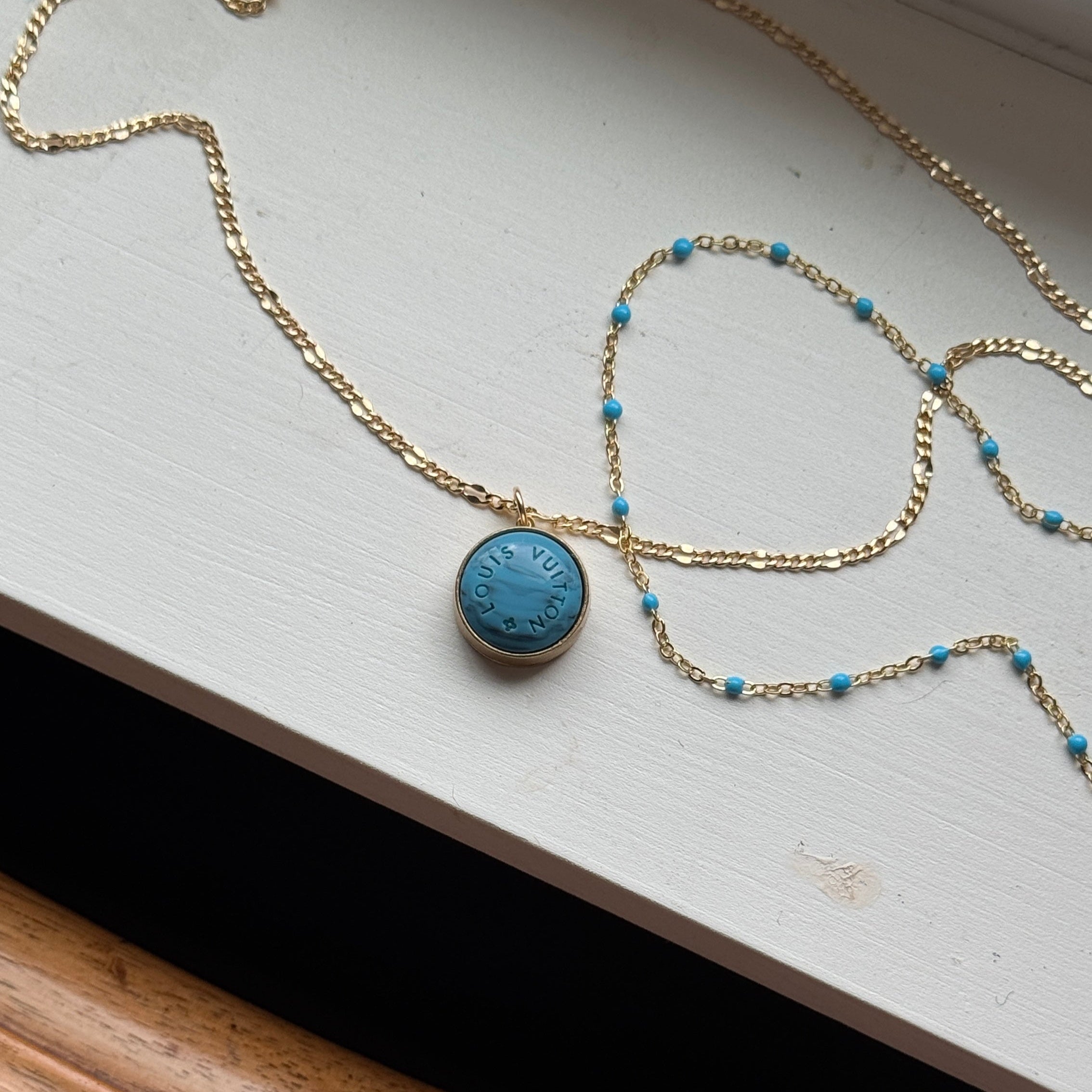 Close-up of a vintage Louis Vuitton turquoise pendant necklace on a matching dainty blue satellite chain. Featuring an authentic repurposed LV charm, this rare piece blends luxury heritage with modern elegance, perfect for layering or wearing solo.