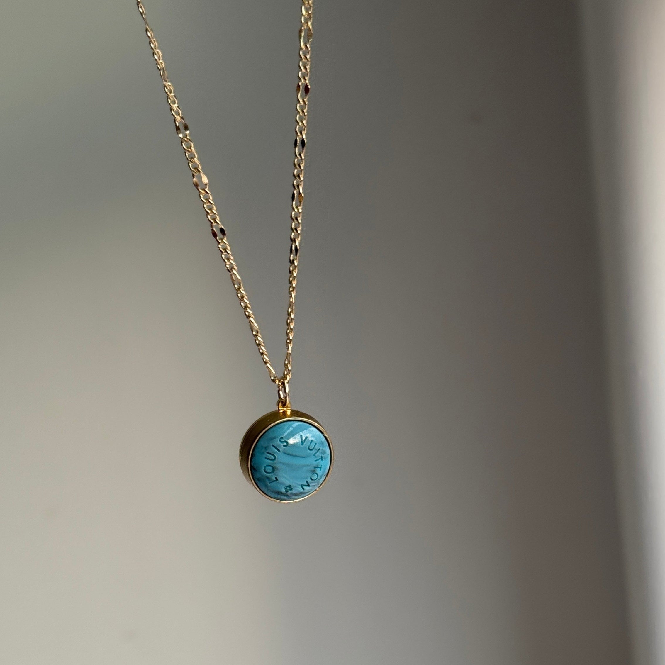 Close-up of a vintage Louis Vuitton turquoise pendant necklace on a matching dainty blue satellite chain. Featuring an authentic repurposed LV charm, this rare piece blends luxury heritage with modern elegance, perfect for layering or wearing solo.