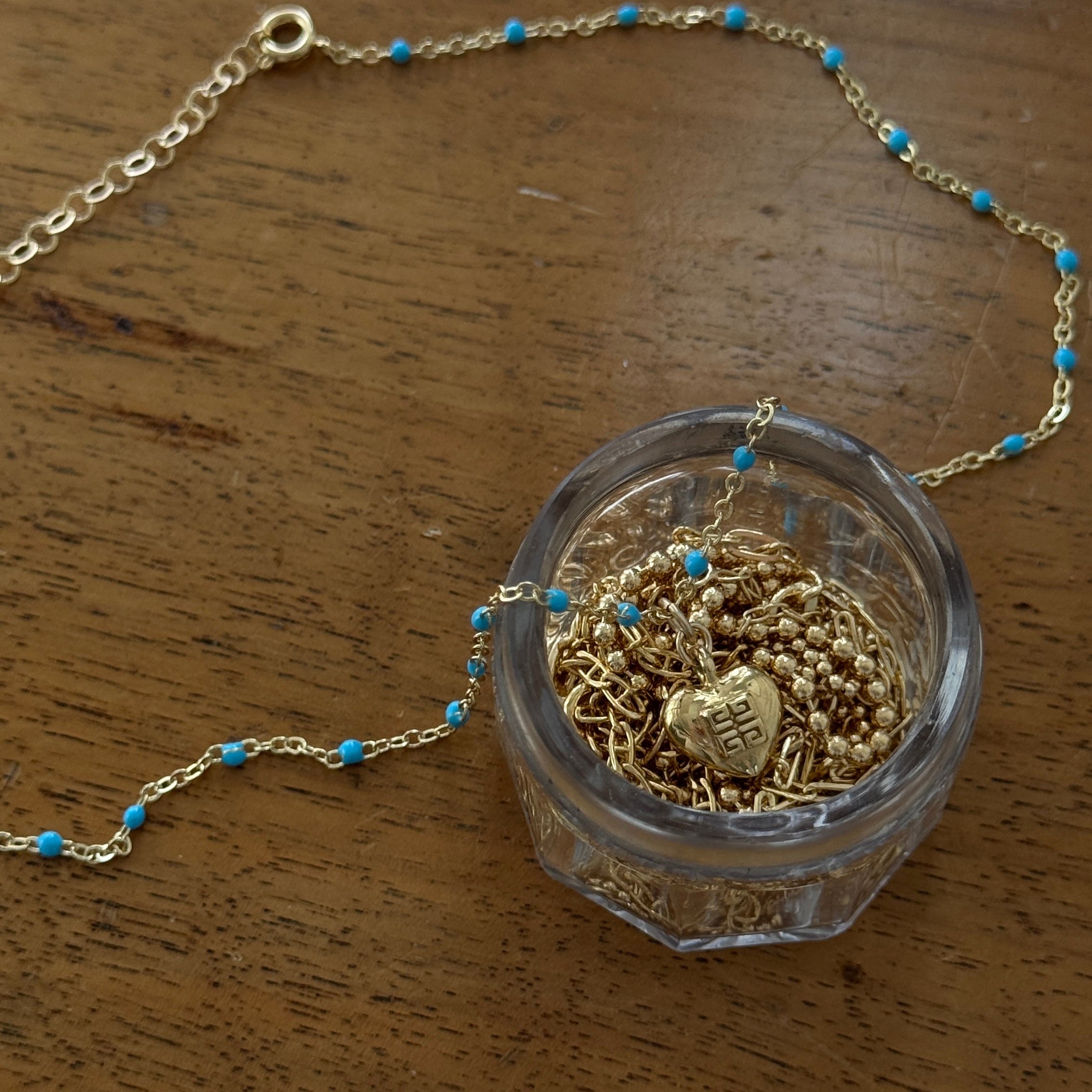 Close-up of a vintage mini Givenchy heart charm necklace, featuring an authentic gold-toned heart pendant on a delicate enamel colored blue chain. A rare and timeless piece, repurposed for modern wear, blending classic elegance with effortless everyday luxury