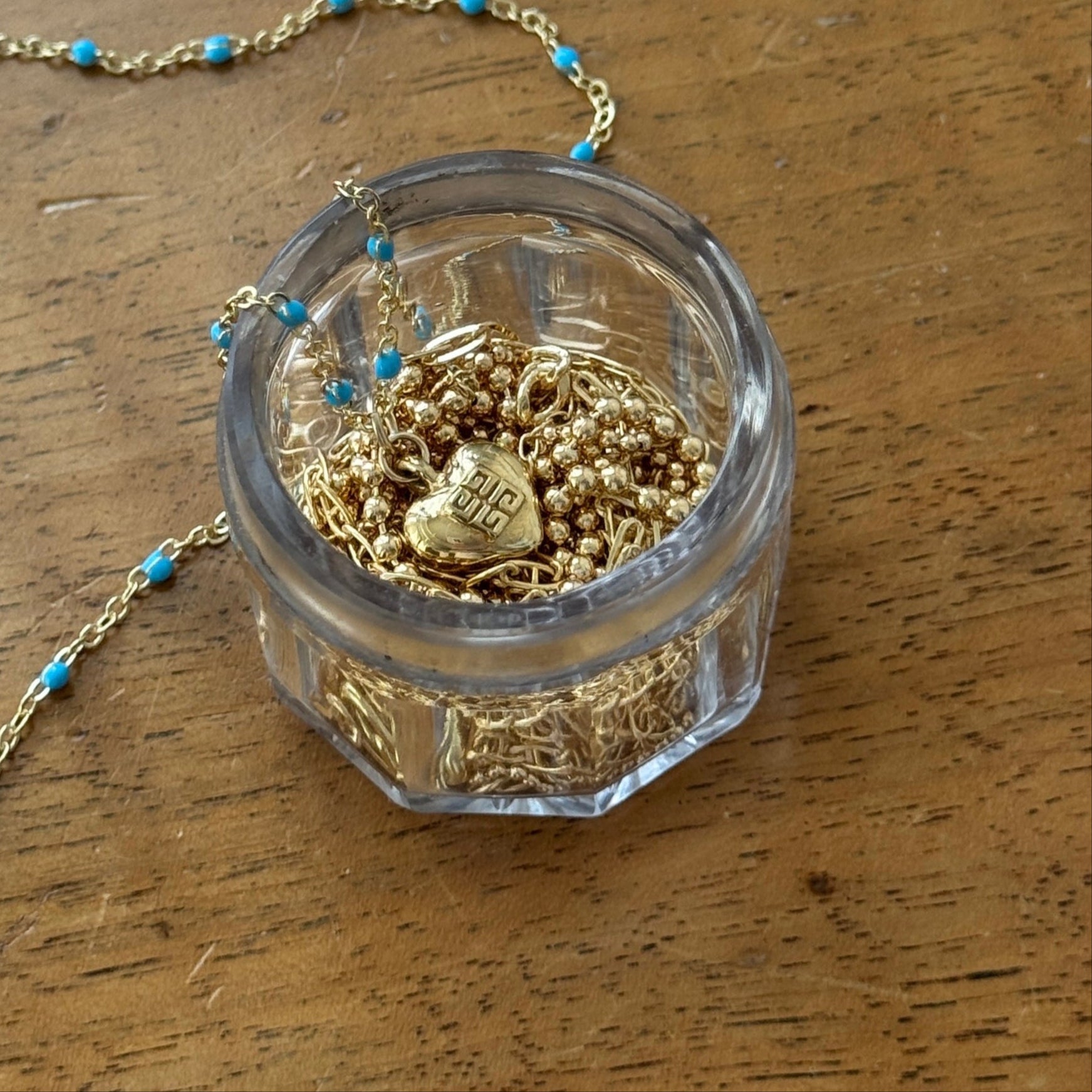 Close-up of a vintage mini Givenchy heart charm necklace, featuring an authentic gold-toned heart pendant on a delicate enamel colored blue chain. A rare and timeless piece, repurposed for modern wear, blending classic elegance with effortless everyday luxury