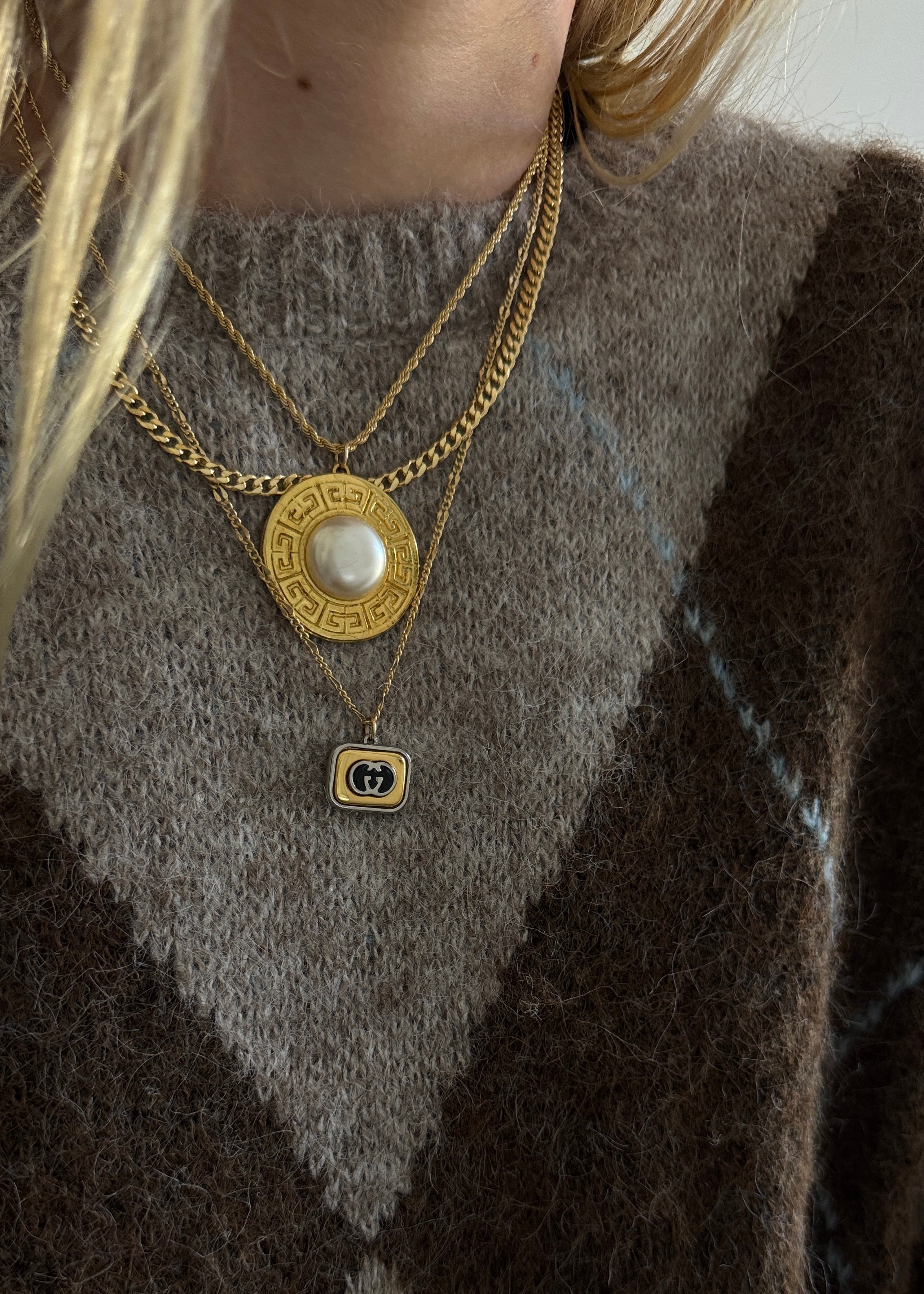 Close-up of a person wearing layered gold vintage Gucci and Givenchy necklaces against a neutral background.